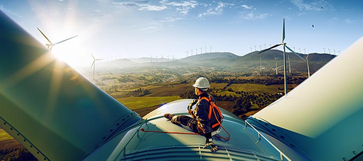 Happy engineer feel success after good work. He standing a top of windmill and looking beautiful sunset